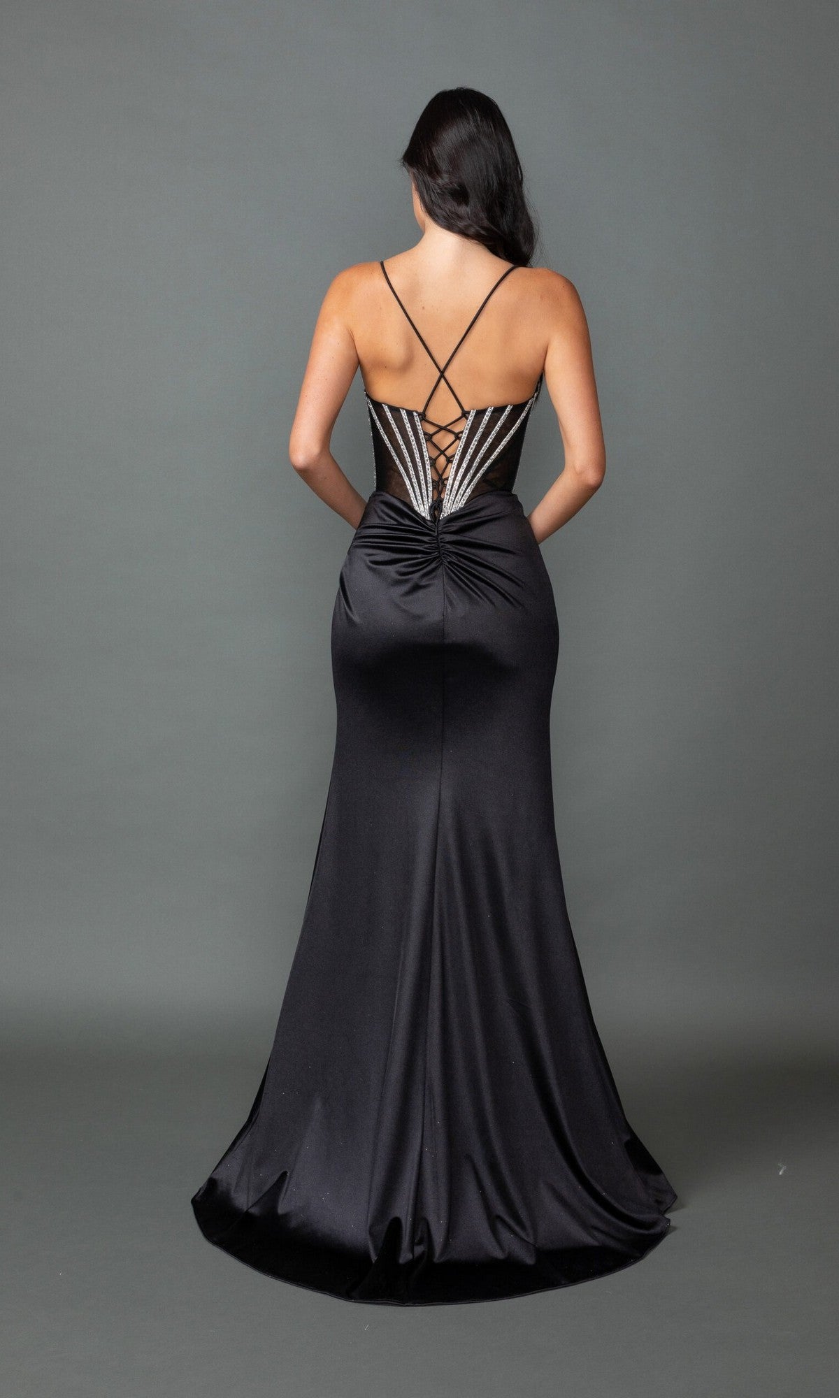 A woman faces away, wearing the Dancing Queen 4538 long prom dress with a black lace-up back, metallic details, and a satin skirt, set against a plain gray background.